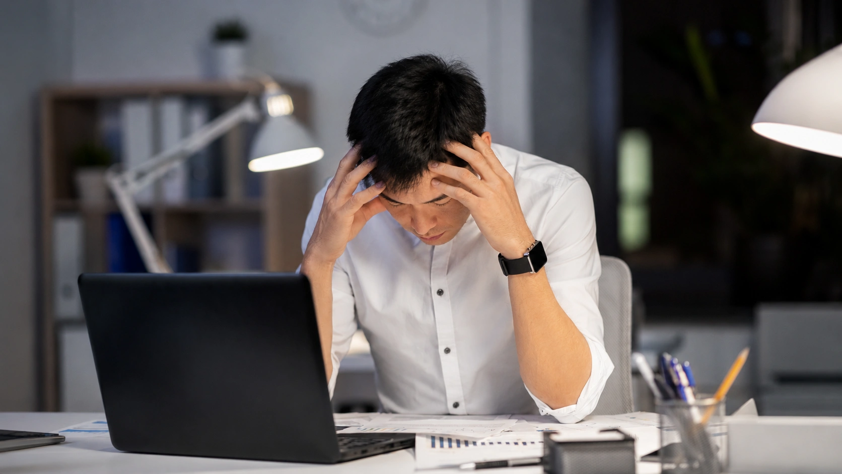 Asian working professional feeling overwhelmed while working on a laptop in an office.